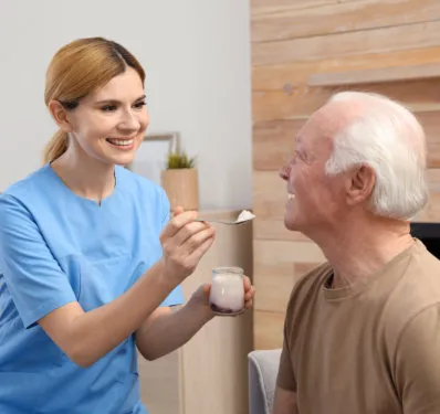 A caregiver in scrubs helping an older man with his meal at home
